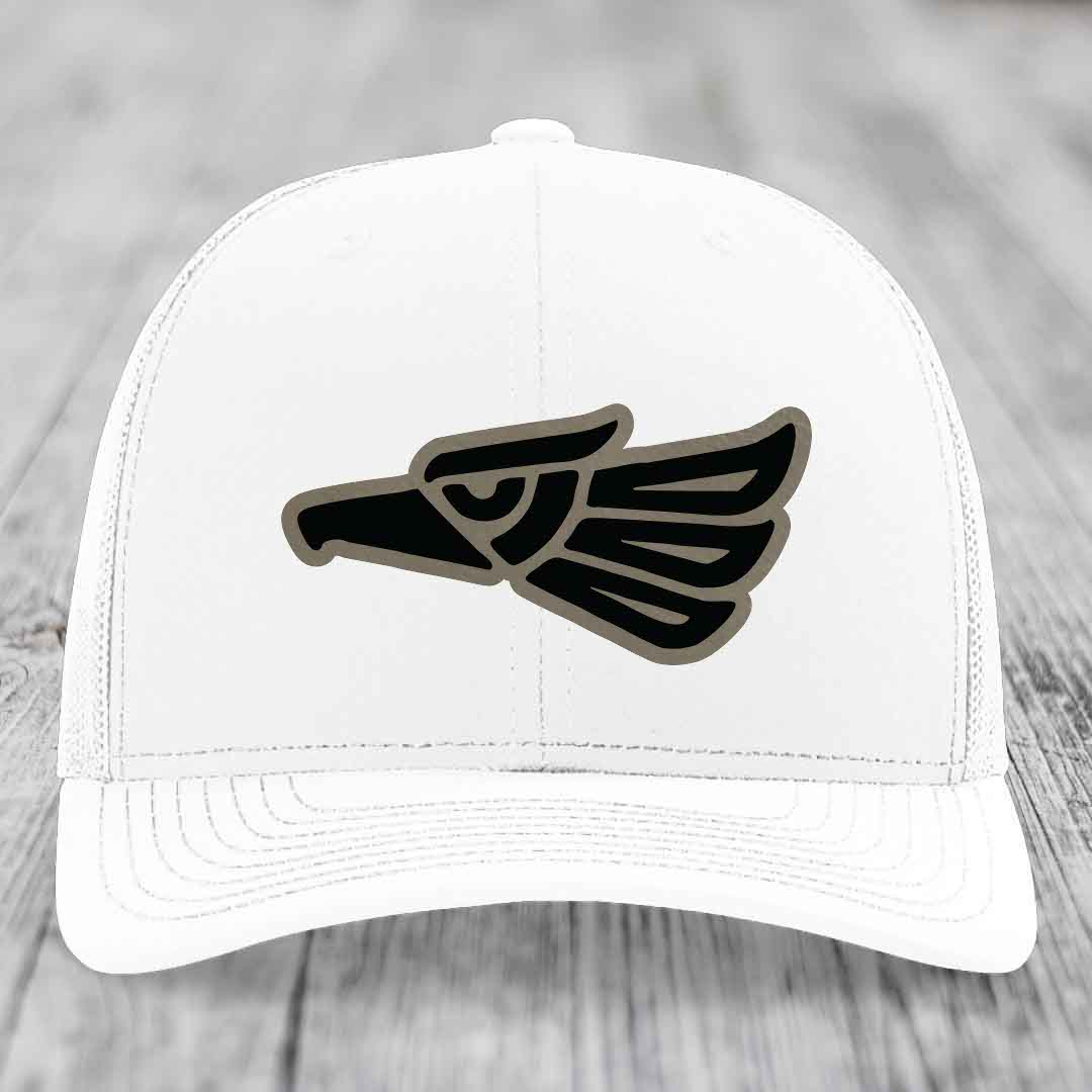 White trucker hat with black and grey Aztec-style eagle patch on front.