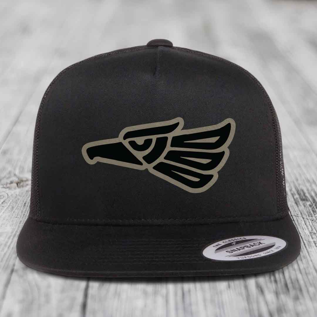 Black snapback hat with Aztec-style eagle patch on front, displayed on wooden surface.