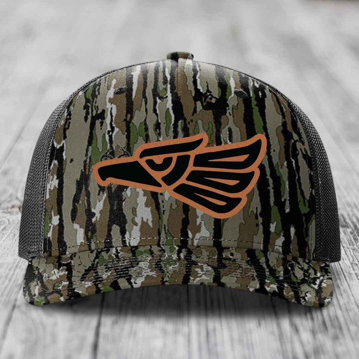 Camouflage trucker hat with black and orange eagle patch on front.