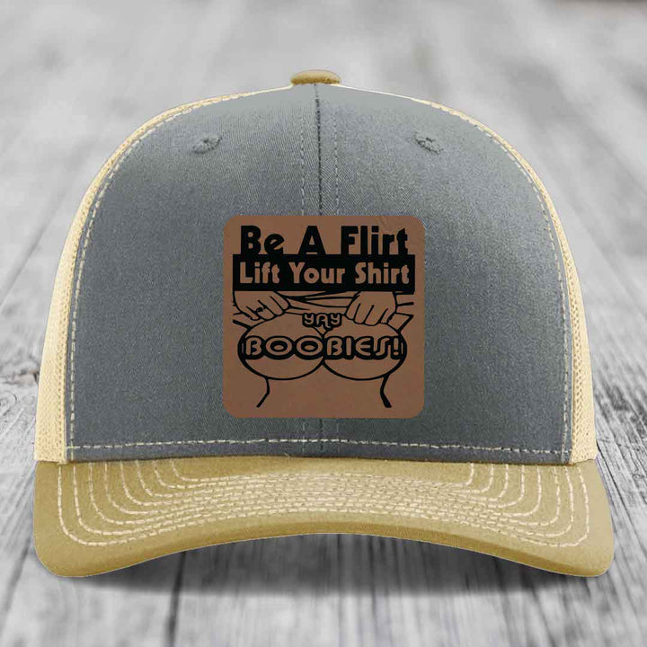 Grey and beige trucker hat with a brown leatherette patch that says &