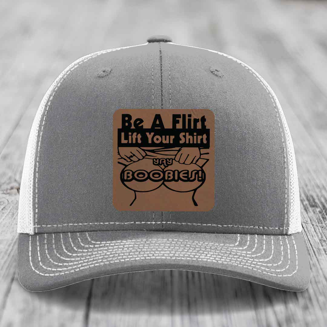 Grey trucker hat with white mesh back and a brown leatherette patch reading &