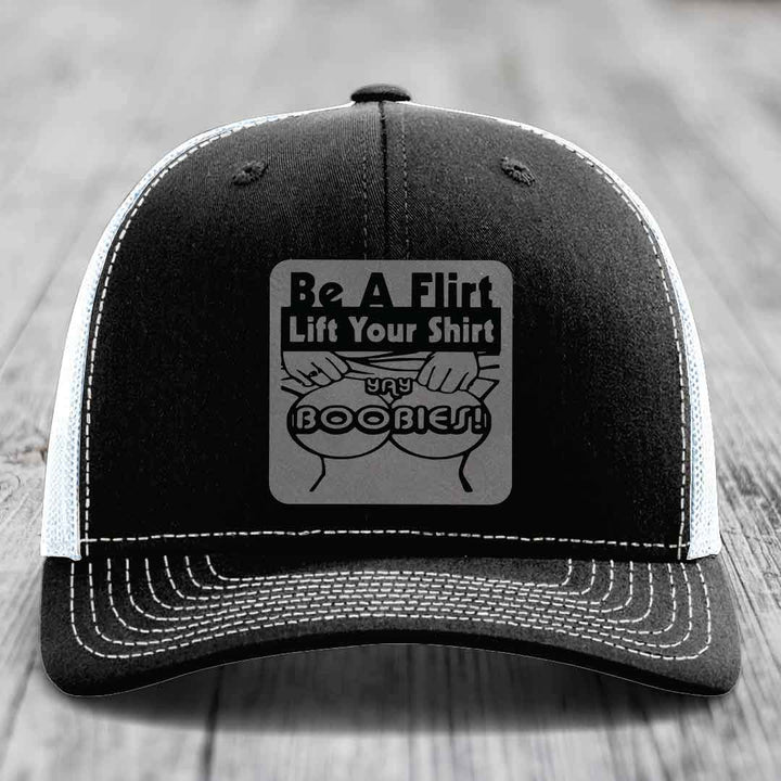 Black trucker hat with white stitching and a gray patch reading &