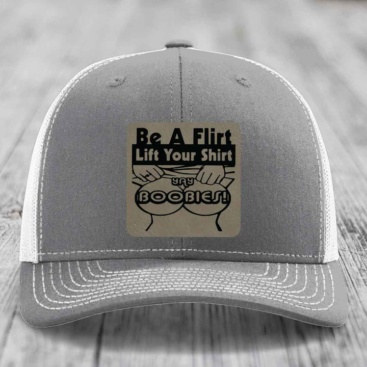 Grey trucker hat with white mesh back and a beige leatherette patch reading &