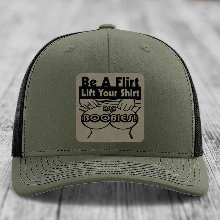 Olive green trucker hat with black mesh back and a beige rectangular patch that reads &