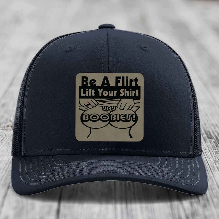 Dark blue trucker hat with a beige leatherette patch reading &