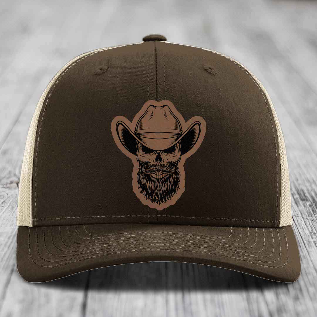 Brown trucker hat with embroidered bearded cowboy skull patch on front.