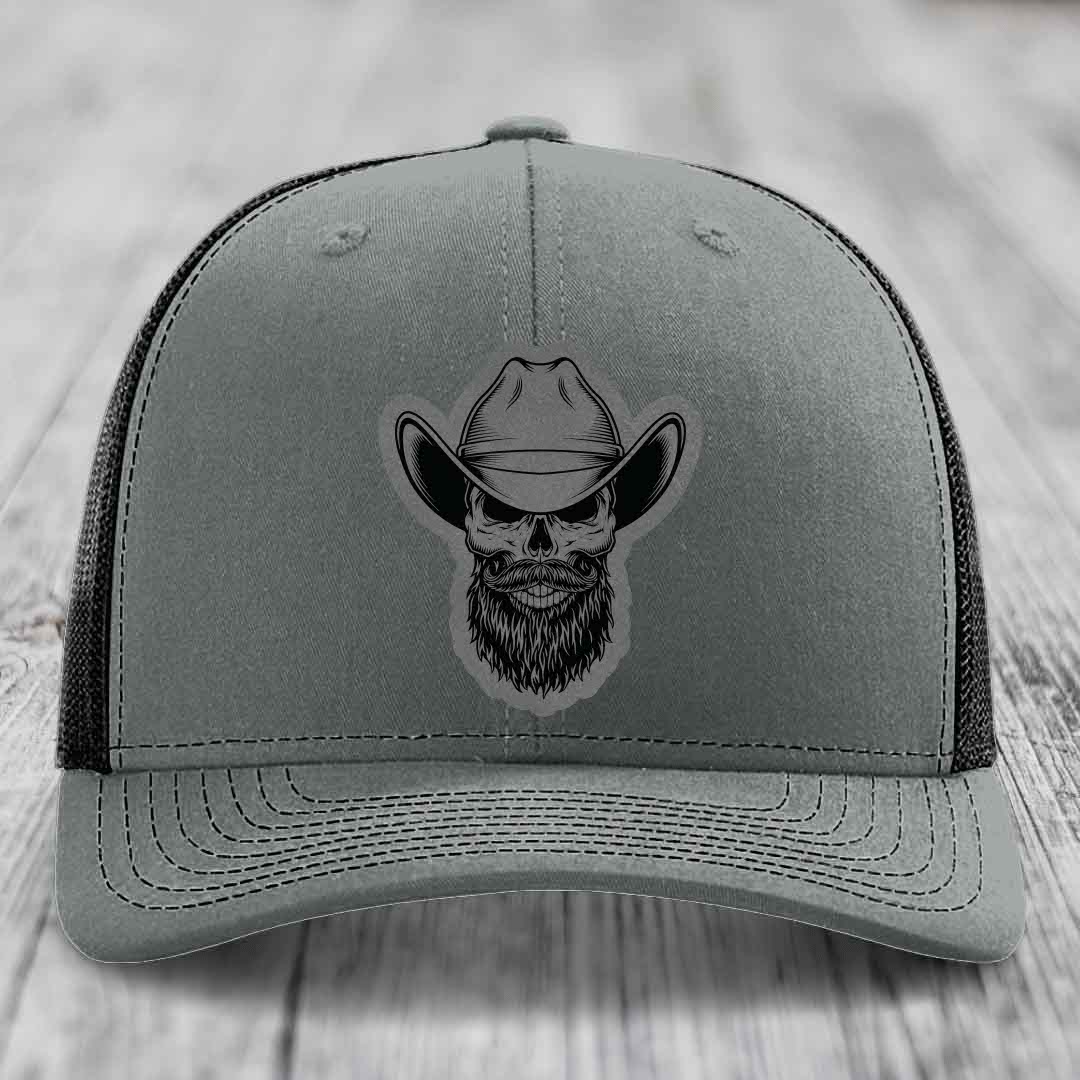 Grey trucker hat with black bearded cowboy skull patch on front.