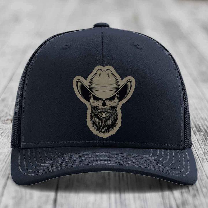 Black trucker hat with beige bearded cowboy skull patch on front.
