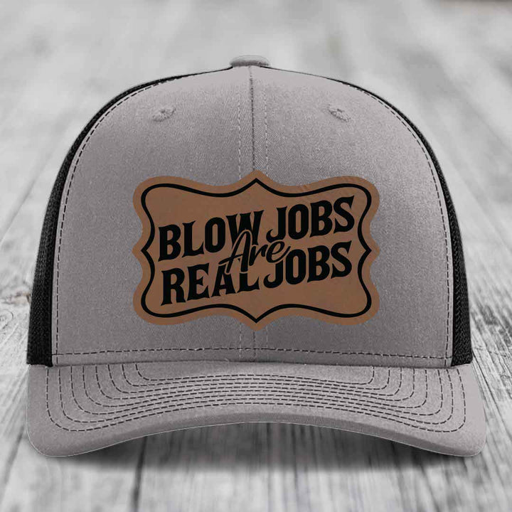 Grey trucker hat with black mesh back and a brown leatherette patch that reads &
