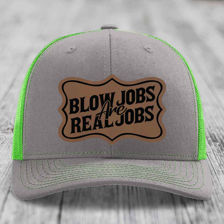 Grey trucker hat with neon green mesh and stitching, featuring a brown leatherette patch that reads &