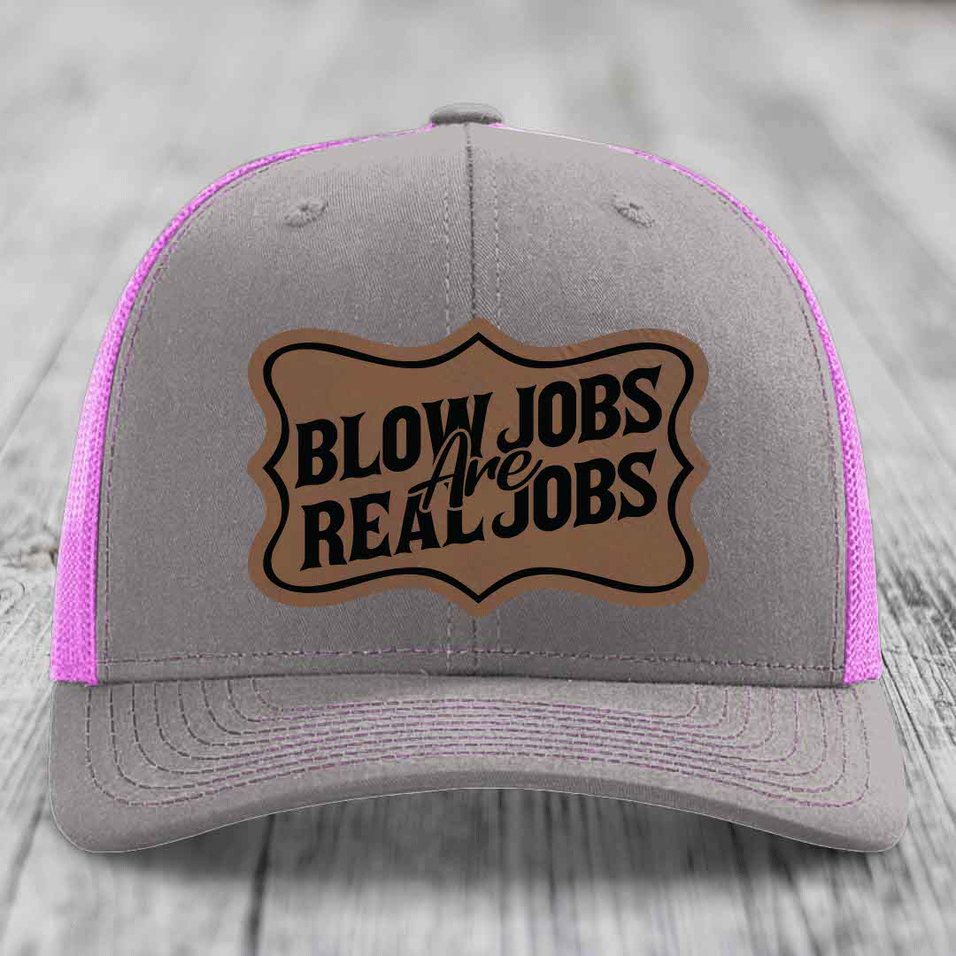 Grey trucker hat with pink mesh sides and a brown leatherette patch reading &