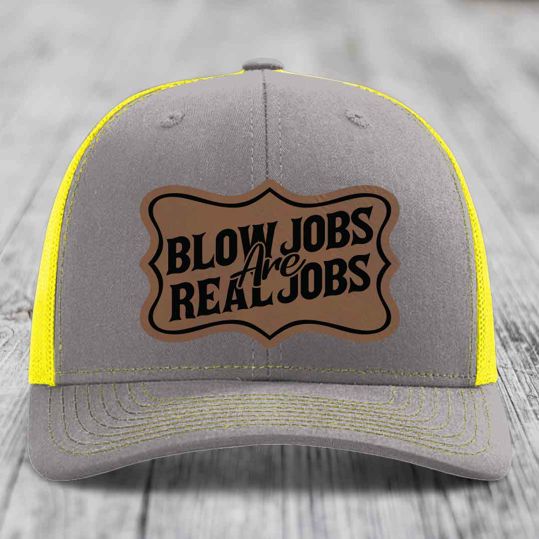 Grey trucker hat with yellow mesh and stitching, featuring a brown leatherette patch that reads &