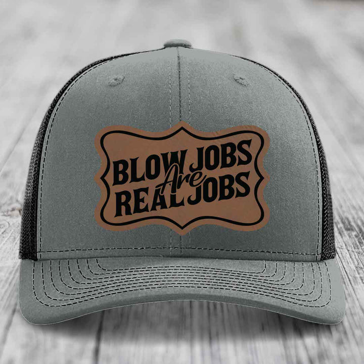 Grey trucker hat with black mesh back and a brown leatherette patch reading &