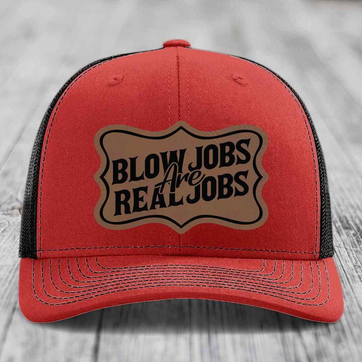 Red trucker hat with black mesh back and a brown leatherette patch that reads &