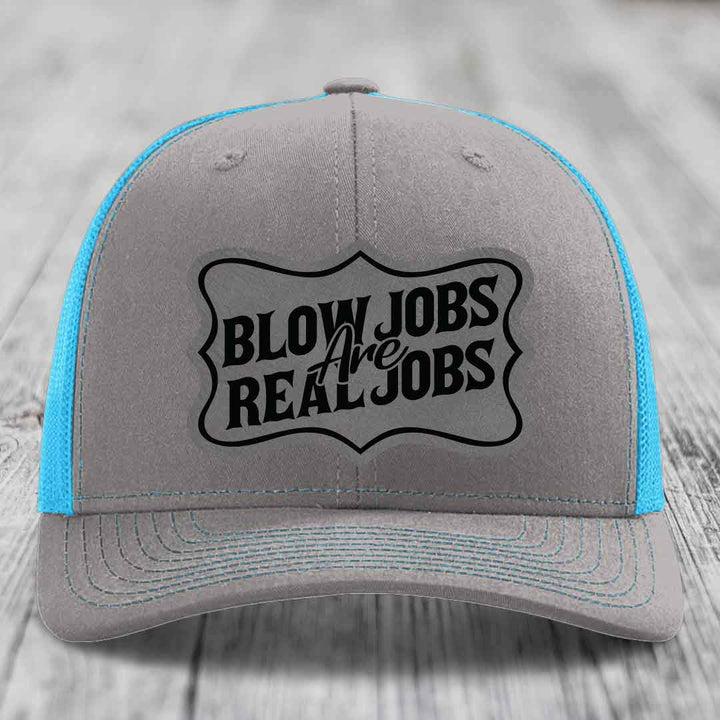 Grey trucker hat with blue mesh sides and black embroidered patch reading &