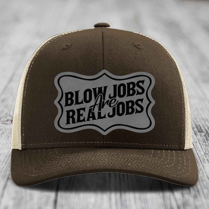 Brown trucker hat with cream mesh back and black embroidered patch reading &