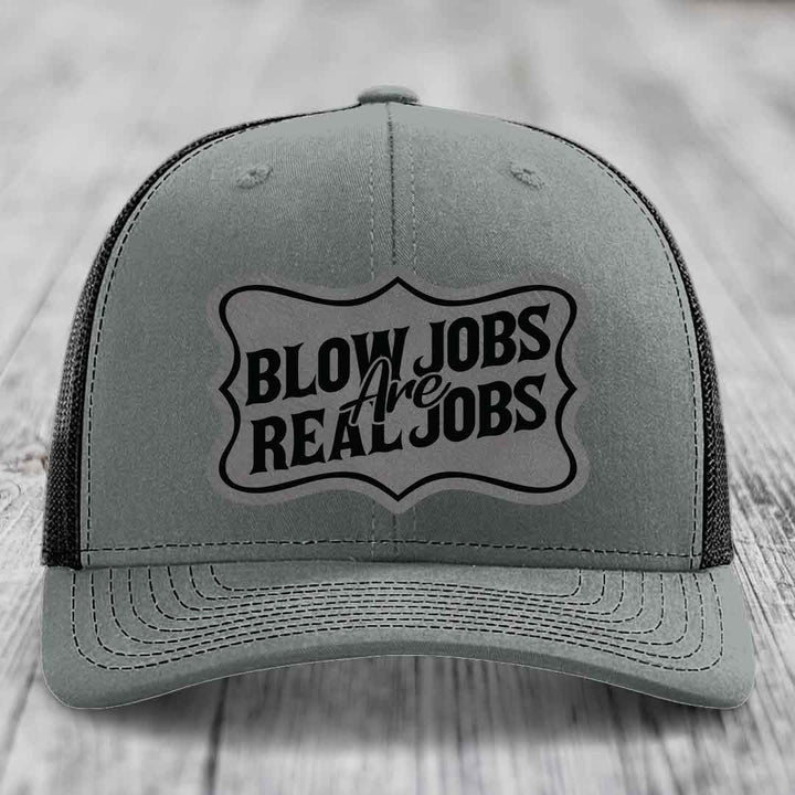 Grey trucker hat with black mesh back and embroidered patch reading &