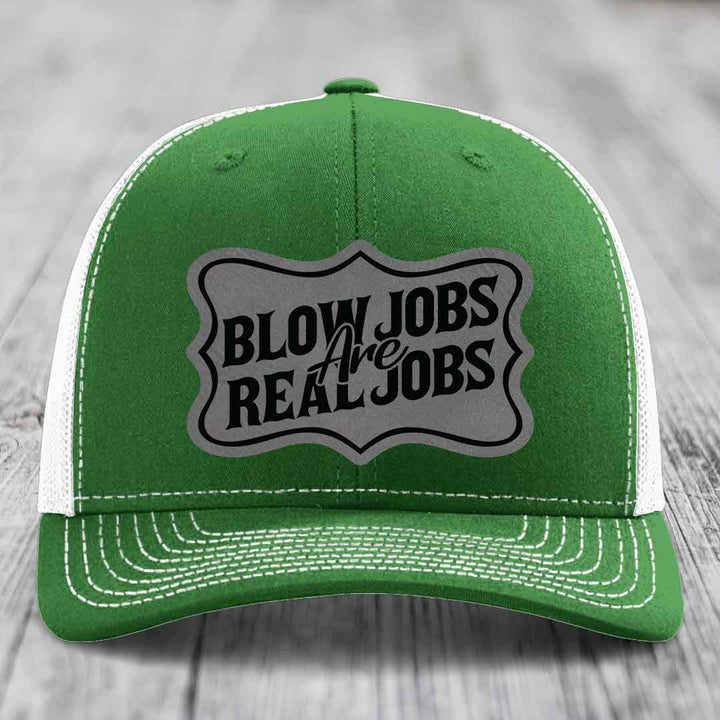 Green trucker hat with white mesh back and stitching, featuring a grey shield patch that reads &