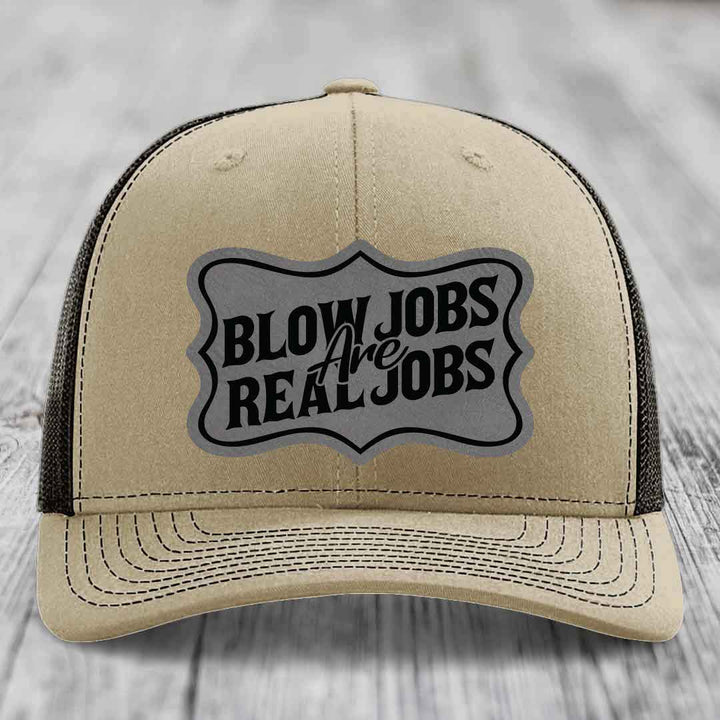 Tan trucker hat with black mesh back and a grey shield patch that reads &