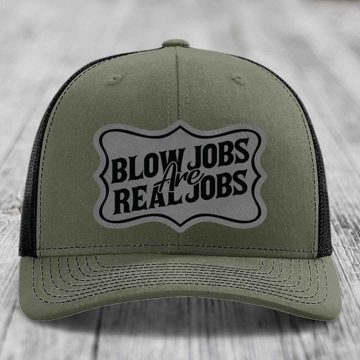 Olive green trucker hat with black mesh back and a grey shield-shaped patch reading &