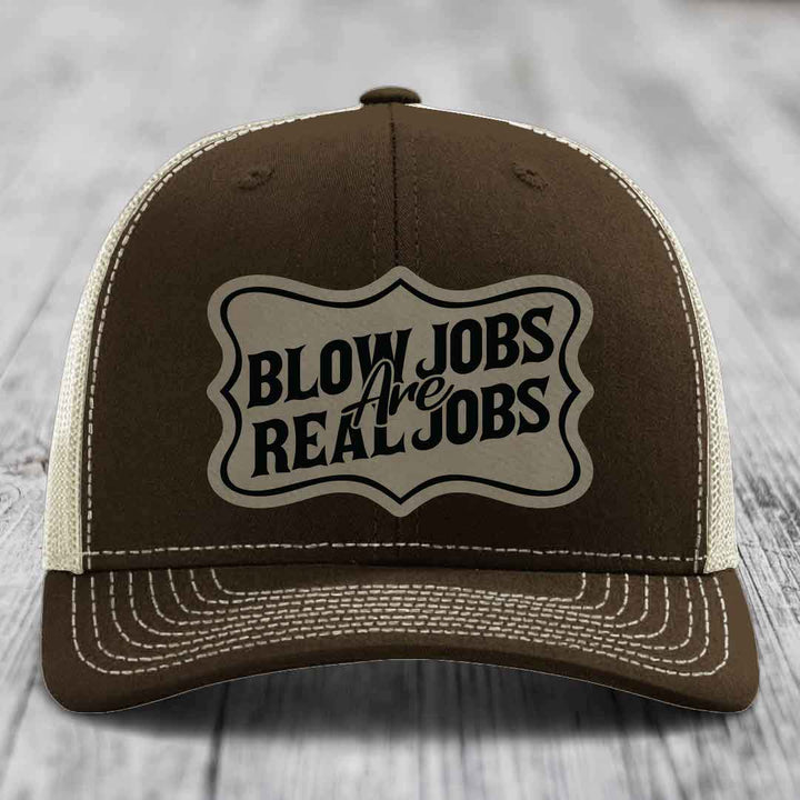 Brown trucker hat with cream mesh back and white stitching, featuring a beige patch that reads &
