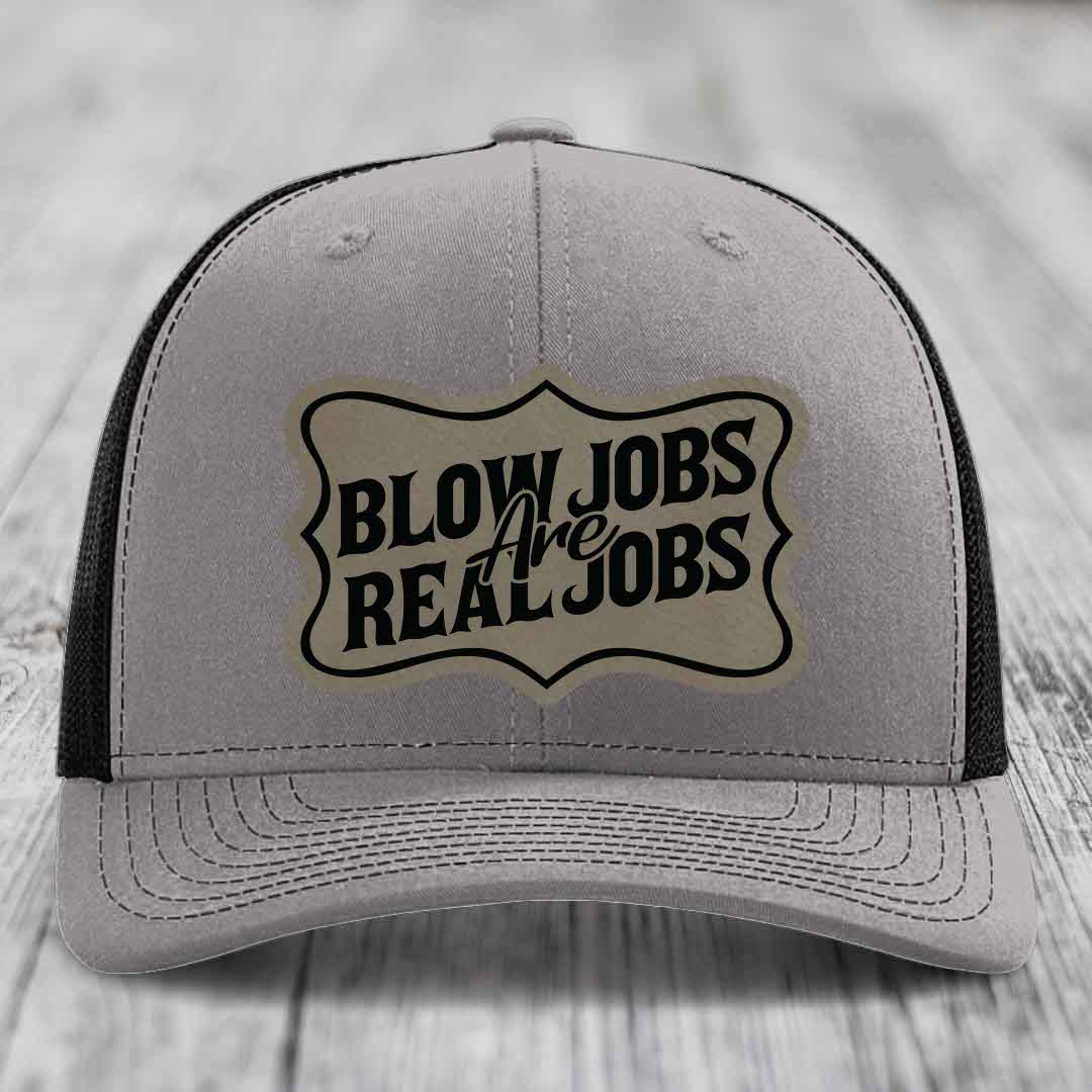 Grey trucker hat with black mesh back and a beige leatherette patch that reads &