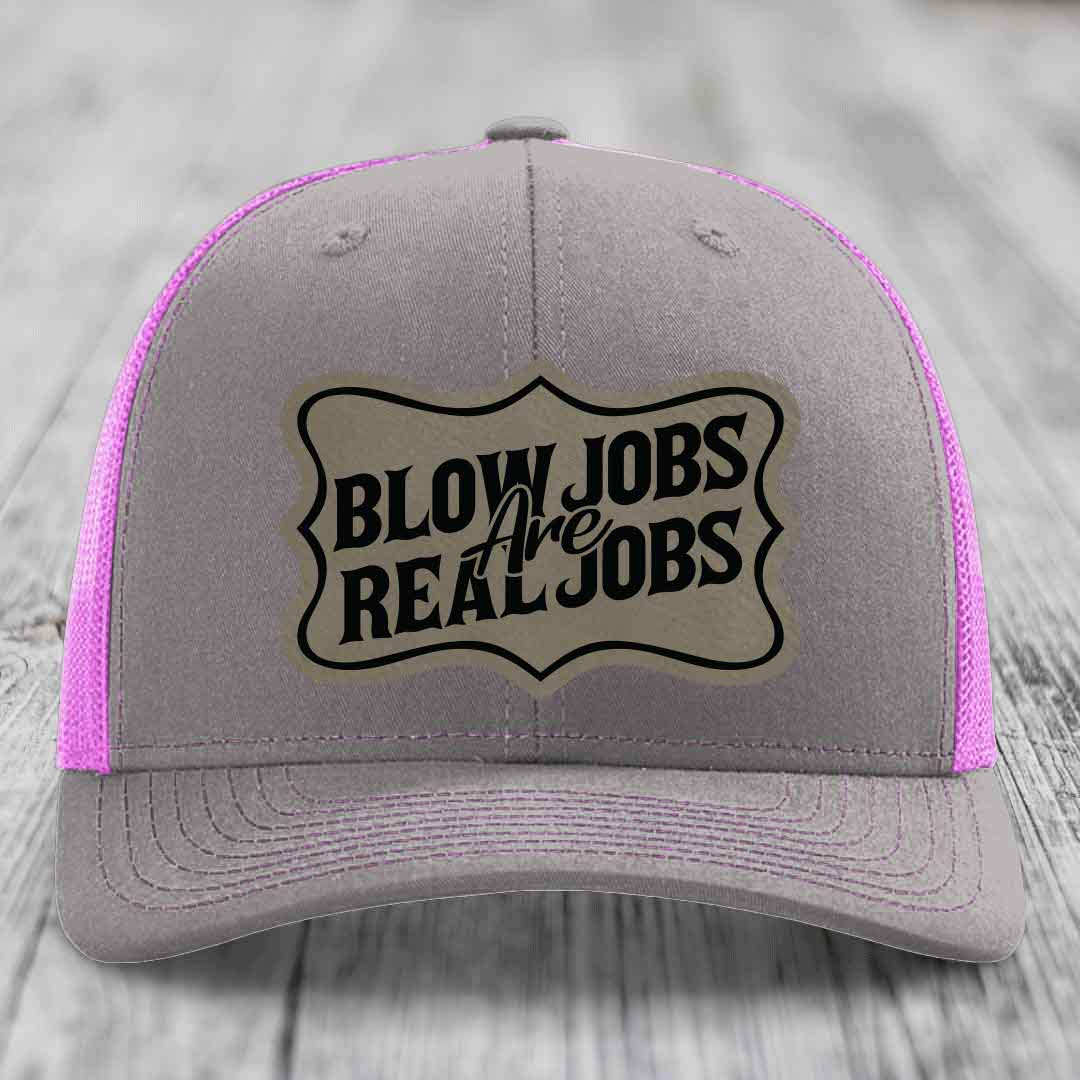 Grey trucker hat with pink mesh sides and a beige leatherette patch that reads &
