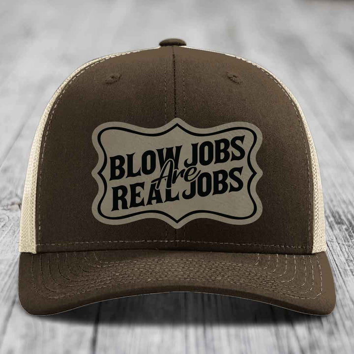 Brown trucker hat with beige mesh back and black embroidered patch reading &