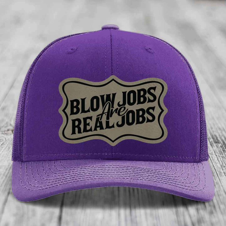 Purple trucker hat with a beige leatherette patch that reads &