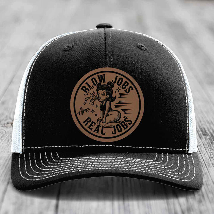 Black trucker hat with white mesh back and stitching, featuring a brown circular leather patch with text and illustration.