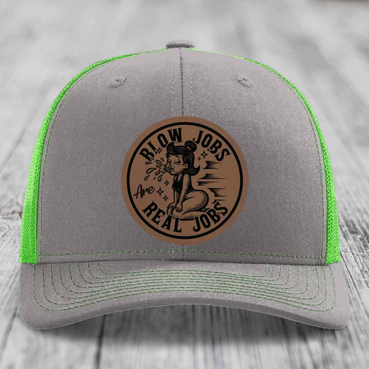 Grey trucker hat with neon green mesh and a brown leather patch that reads &