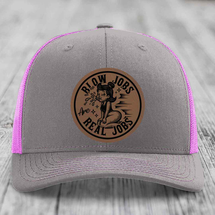 Grey trucker hat with pink mesh, featuring a brown leatherette patch that reads &