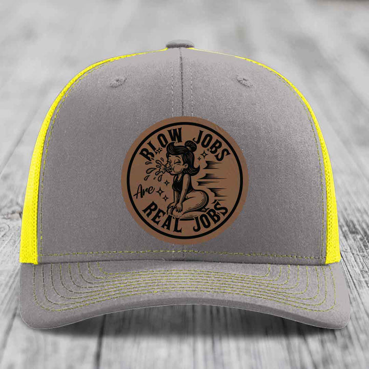 Grey trucker hat with yellow mesh panels and a brown leatherette patch reading &