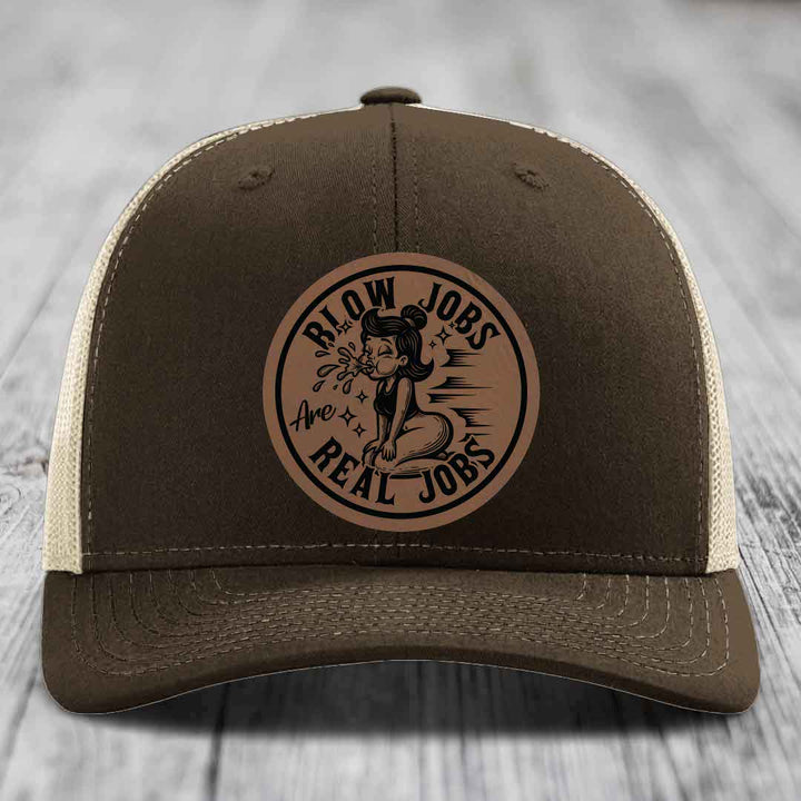 Brown trucker hat with beige mesh back and a circular leatherette patch reading &