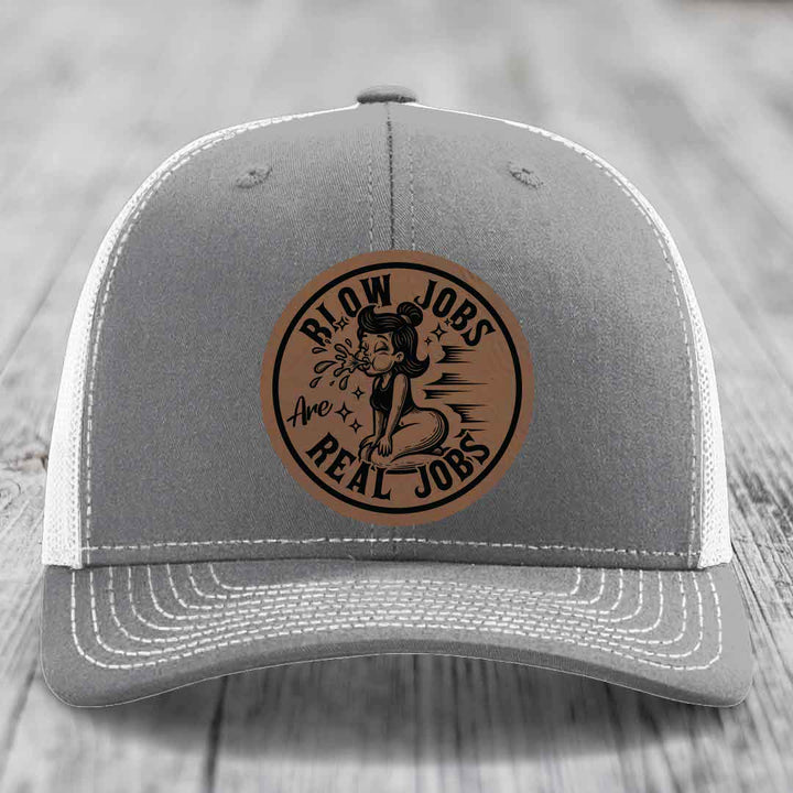 Grey trucker hat with white mesh back and a brown leatherette patch featuring a cartoon woman blowing bubbles and the text &