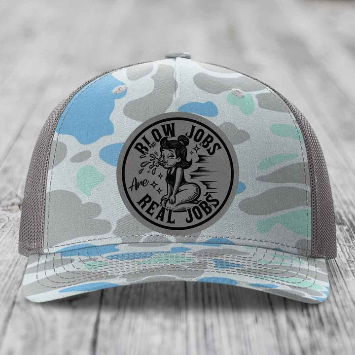 Camouflage trucker hat with a circular black patch reading &