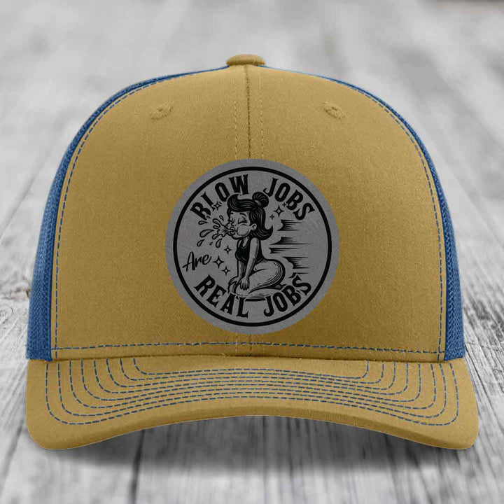 Tan and blue trucker hat with a circular gray patch featuring a cartoon woman blowing bubbles and the text &
