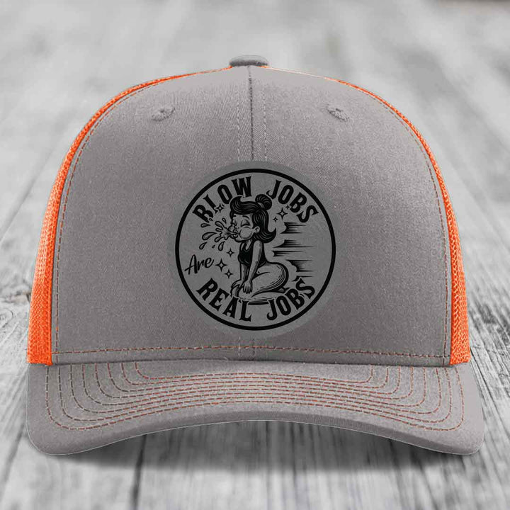 Grey trucker hat with orange mesh back and black circular patch reading &