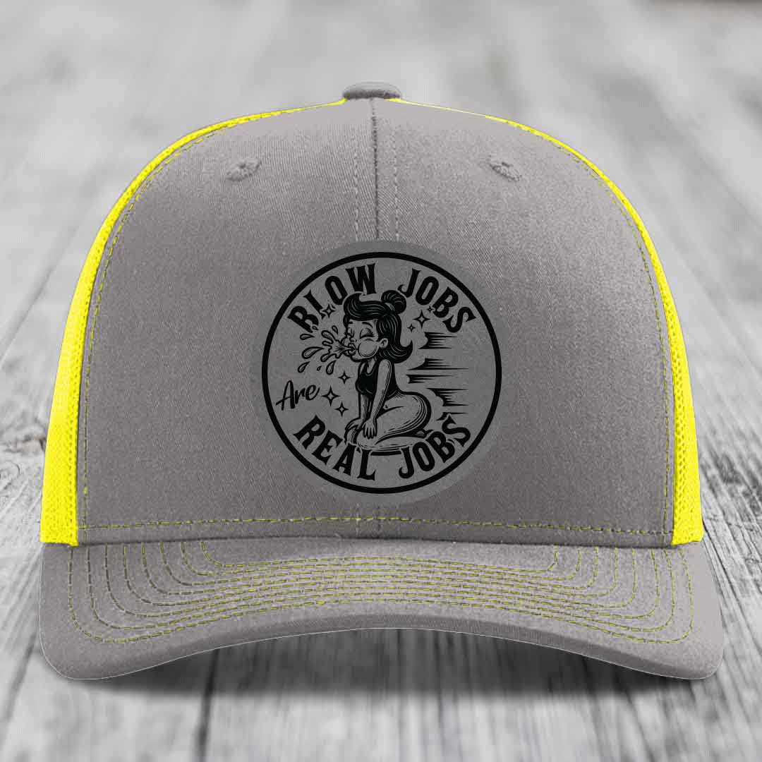 Grey trucker hat with yellow mesh and stitching, featuring a black circular patch that reads &