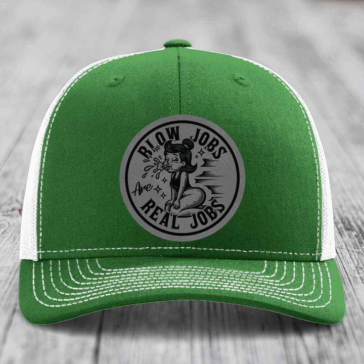 Green trucker hat with white mesh back and stitching, featuring a circular grey patch with black text and illustration.