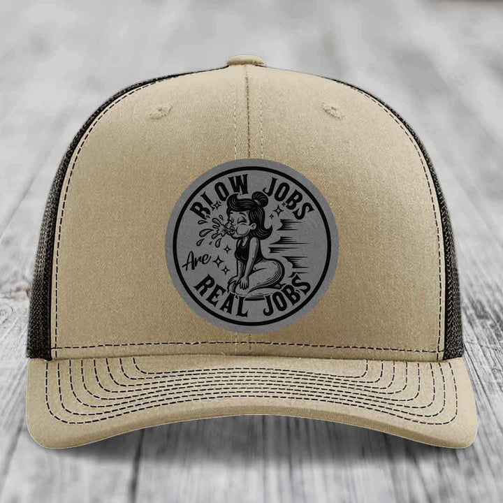 Tan trucker hat with black mesh back and gray circular patch reading &