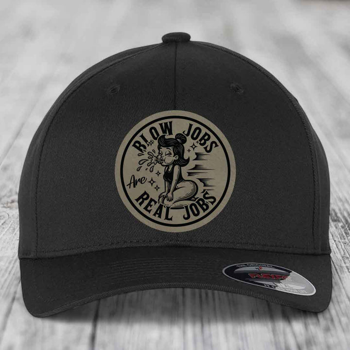 Black baseball cap with circular beige patch featuring cartoon woman and text &