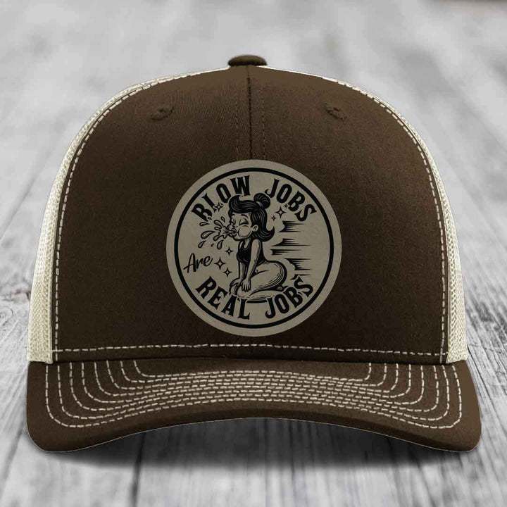 Brown trucker hat with cream mesh back and white stitching, featuring a circular patch that reads &