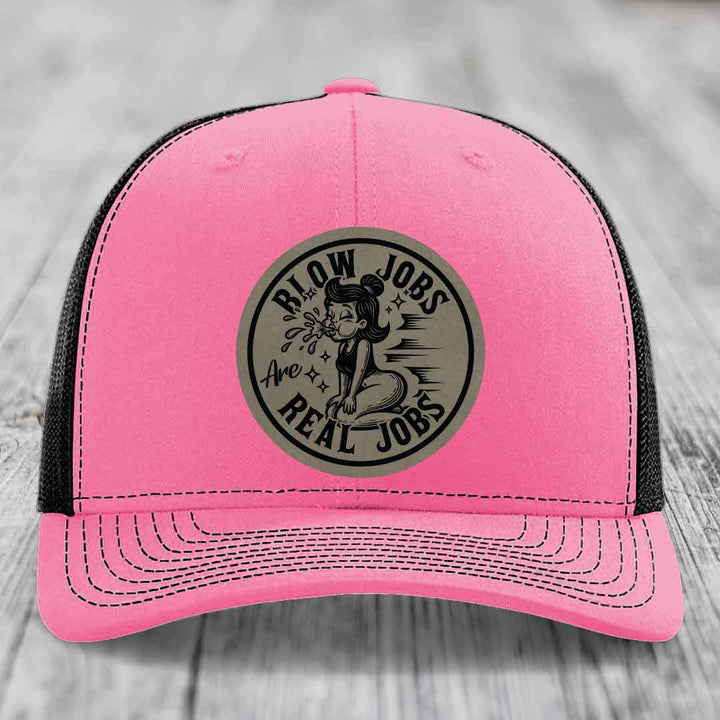Pink trucker hat with black mesh back and gray circular patch reading &
