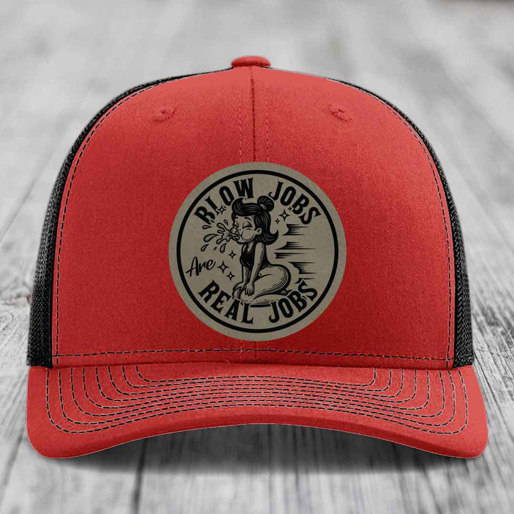 Red trucker hat with black mesh back and a circular beige patch that reads &