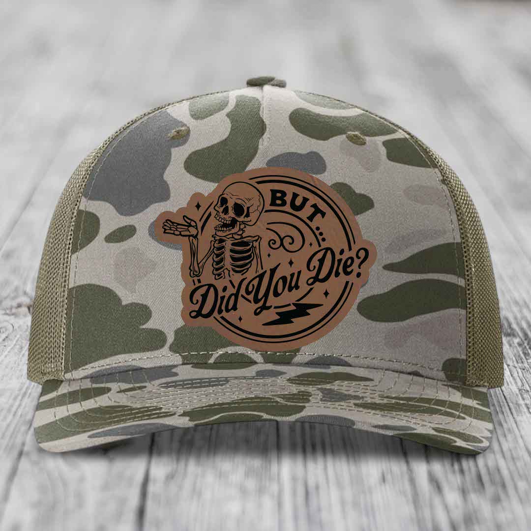 Camouflage trucker hat with brown leather patch featuring skeleton and text &