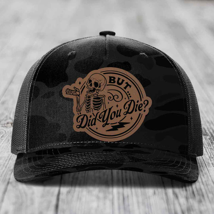 Black camouflage trucker hat with a brown leather patch featuring a skeleton and the text &