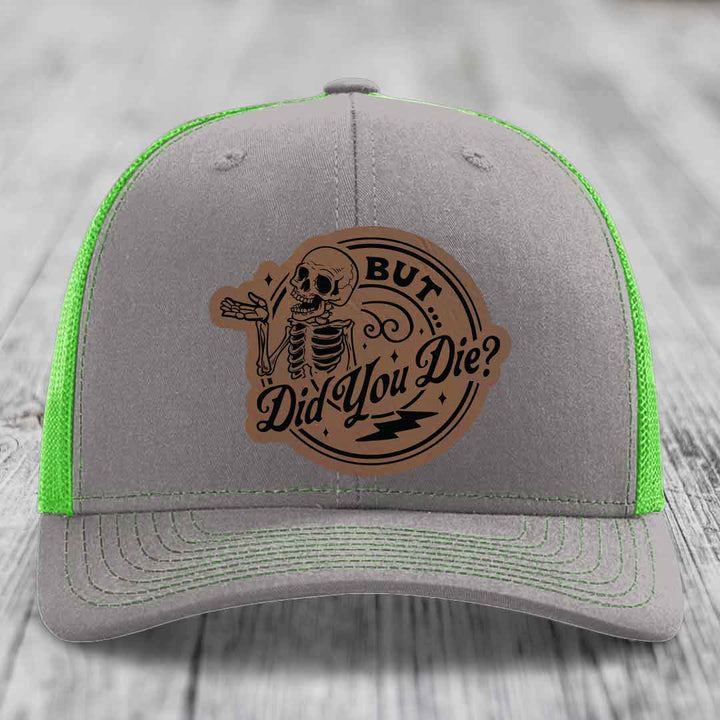 Grey trucker hat with neon green mesh and stitching, featuring a brown leatherette patch with a skeleton and text &