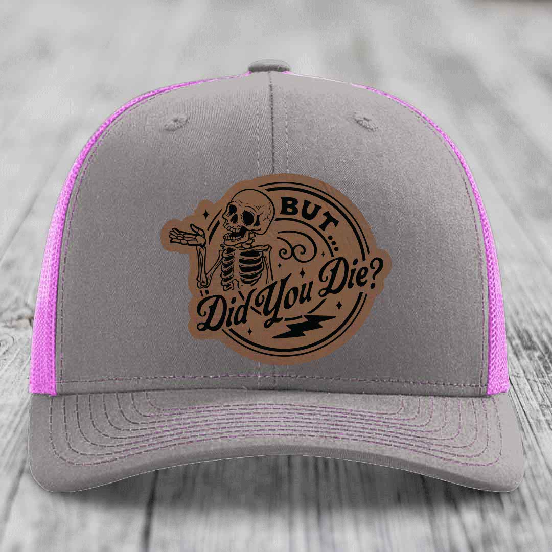 Grey trucker hat with pink mesh and a brown leatherette patch featuring a skeleton and the text &