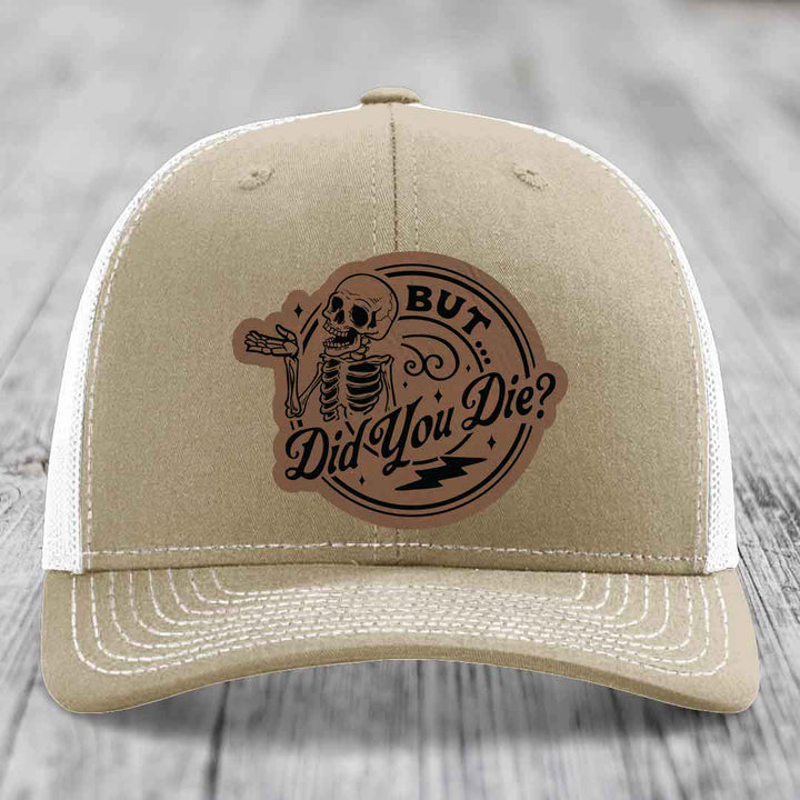 Tan trucker hat with a brown leatherette patch featuring a skeleton and the text &